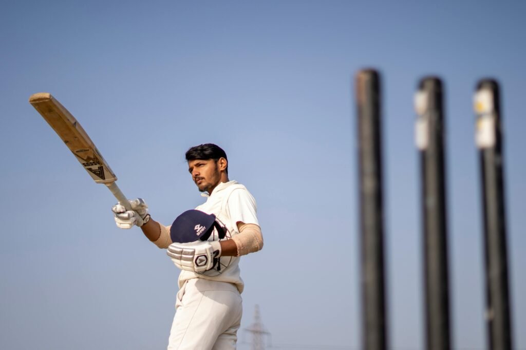 A cricket player in uniform poses with a bat on an outdoor field, ready for action.